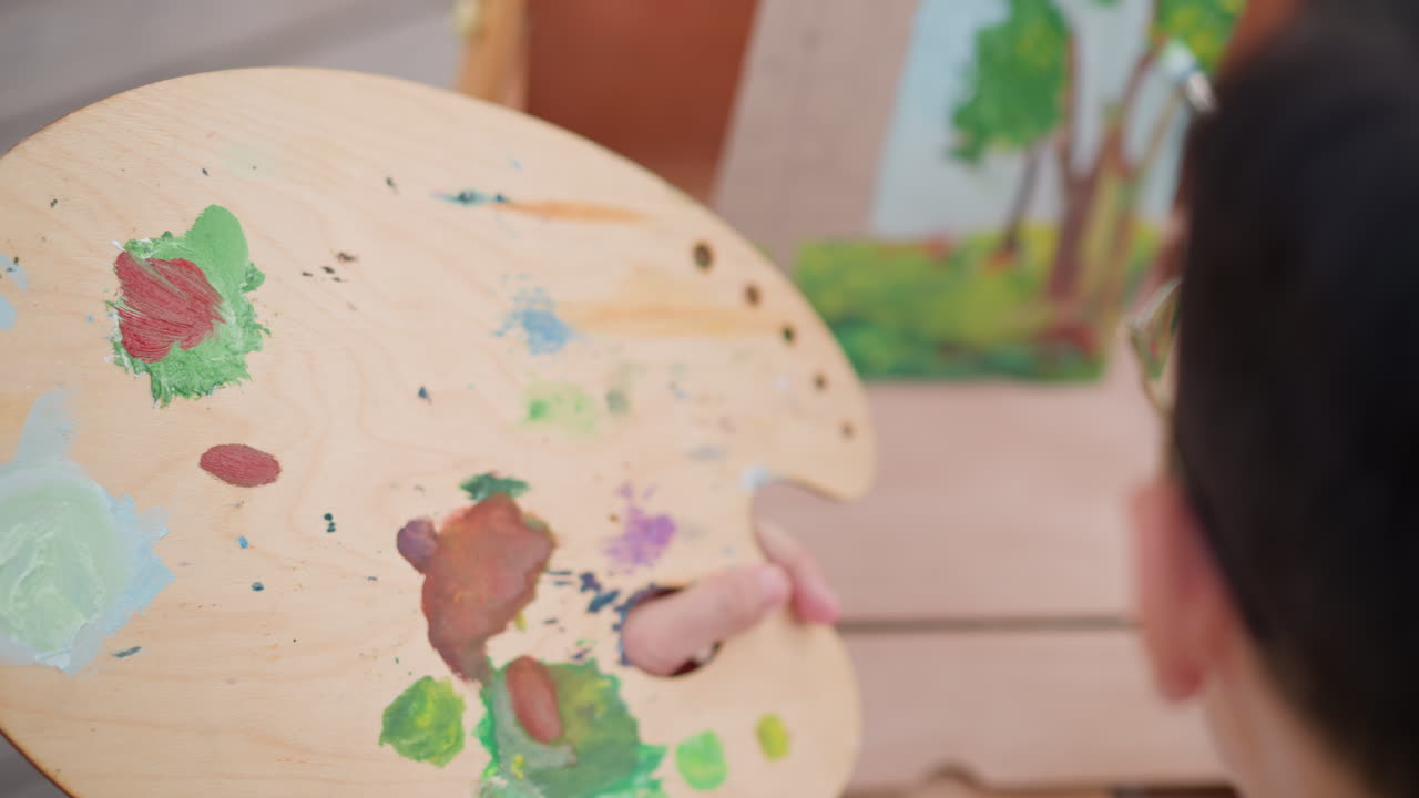 close-up de paleta misturando tinta vermelha com a mão aplicando o pincel, pintor misturando pigmentos quentes em um esboço floral na tela, ambiente de deck ao ar livre com luz natural, técnica de pincelada rápida e criativa