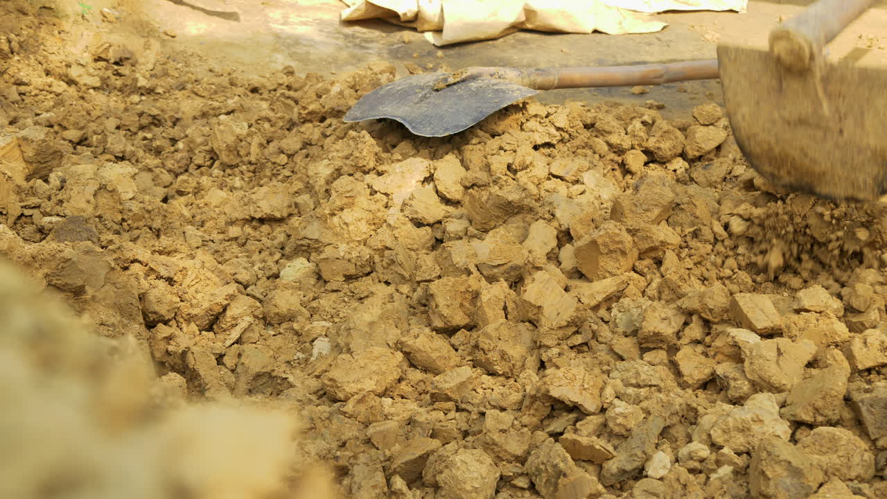 한 남자가 괭이로 진흙 흙을 부수고 탄하에서 전통 아시아 도자기를 준비합니다.