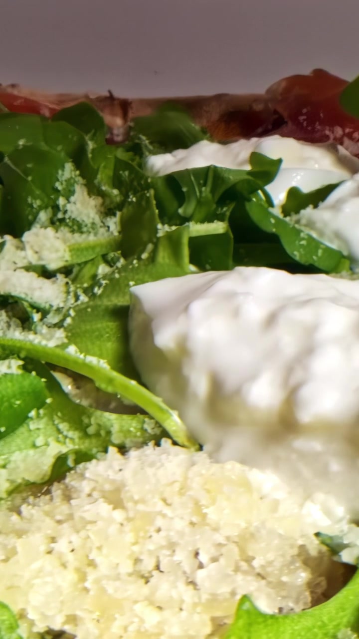 Primo piano di una pizza gourmet guarnita con rucola fresca, burrata cremosa e scaglie di parmigiano. Ideale per blog di cucina o promozioni culinarie.