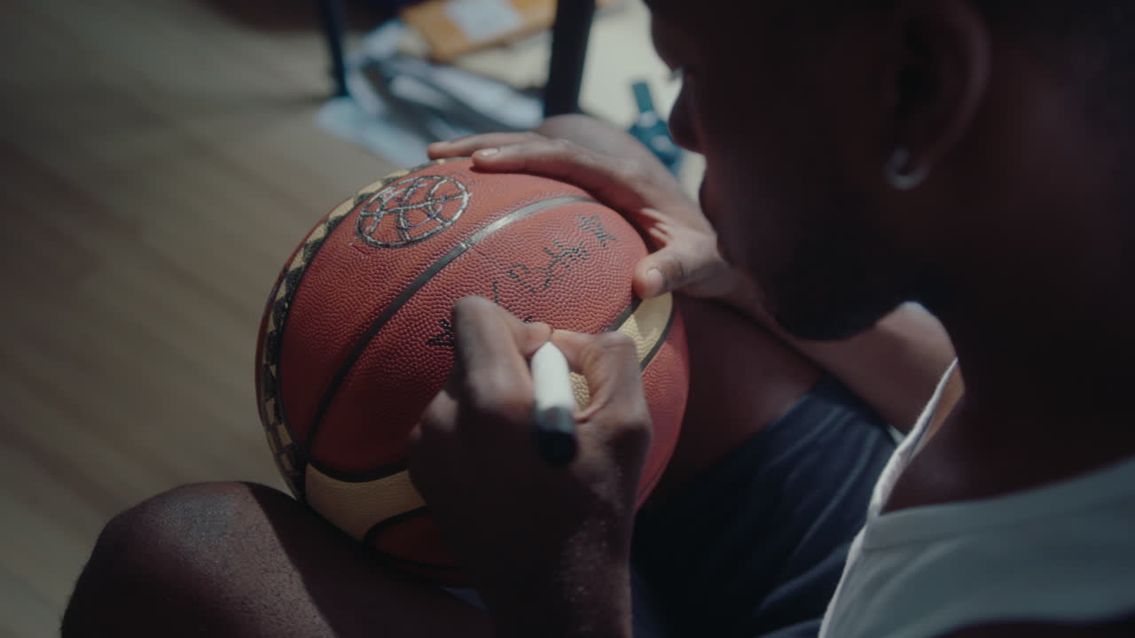 African American Basketball Player Writing a Sign on Ball