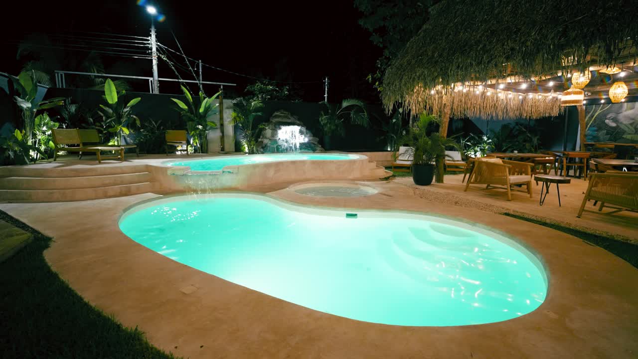 Tropisk resort swimmingpool og vandfald oplyst om natten
