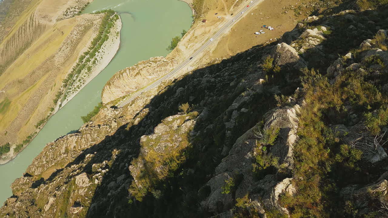 río y campamento en el fondo de la montaña drone fpv lecho del río sinuoso cerca de la carretera y la base turística en las tierras altas alto acantilado empinado en el valle soleado