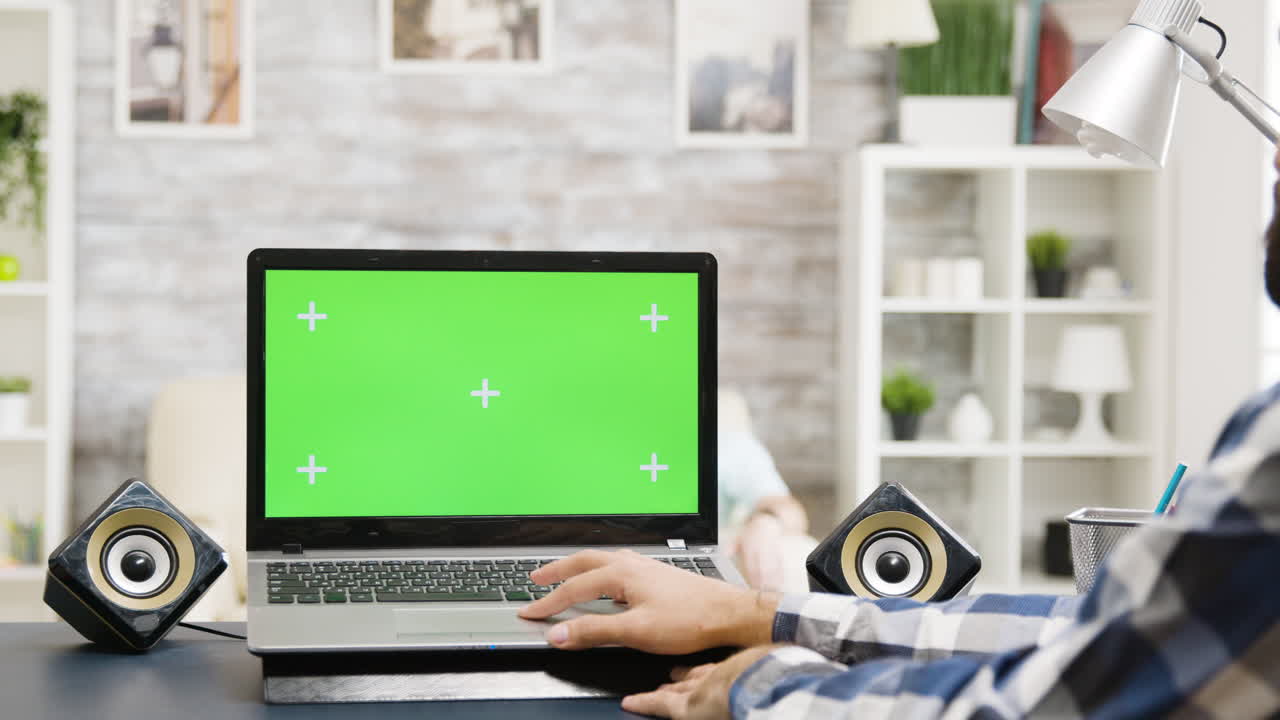 Laptop with green screen and speakers on desk