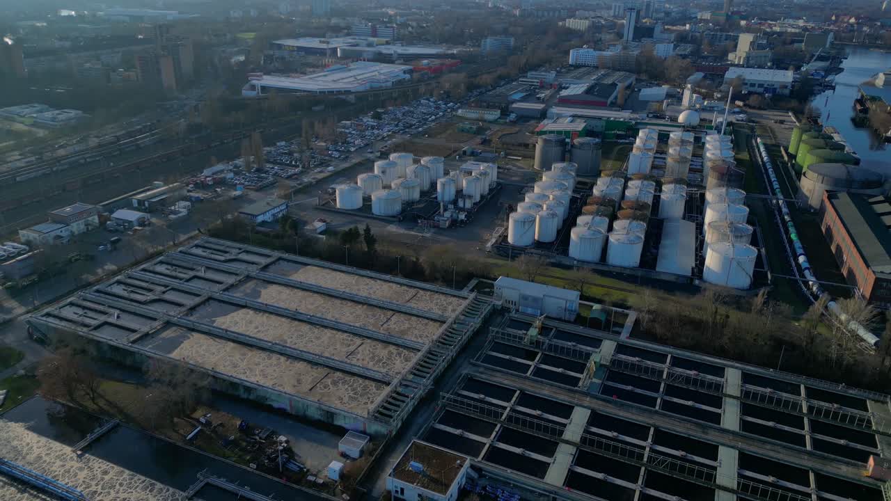 Berlin biogas plant with its large white tanks reflecting on the river next to it during sunset. Magic aerial view flight fly reverse drone
