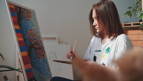 a red haired young female artist mixing colors on a painter's palette and painting a canvas