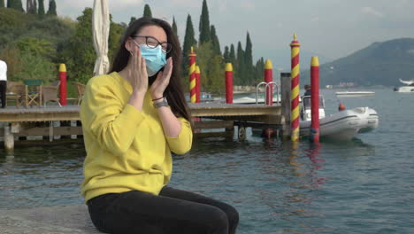 handheld shot of young, caucasian woman in a scenic location putting her covid mask on and smiling at the camera