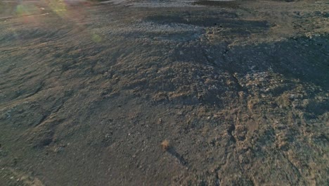 fast, low aerial downward view, pulling away from dry, barren mudstone embankments in a desert