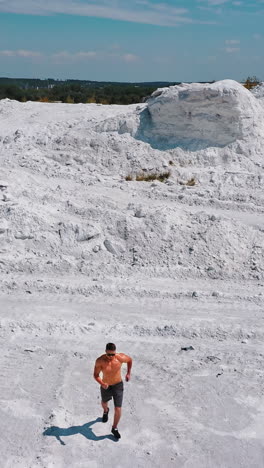 shirtless athlete on white mountain. active sportsman on white natural rocky background. healthy bodybuilder under blue sky. aerial view. motion camera back down. vertical video