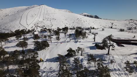 Vista-Aérea-De-Una-Estación-De-Esquí-En-La-Cima-De-La-Colina-Que-Revela-Las-Montañas-Nevadas-Detrás