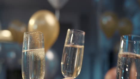 Friends-holding-up-champagne-flutes-together-in-a-toast-at-party