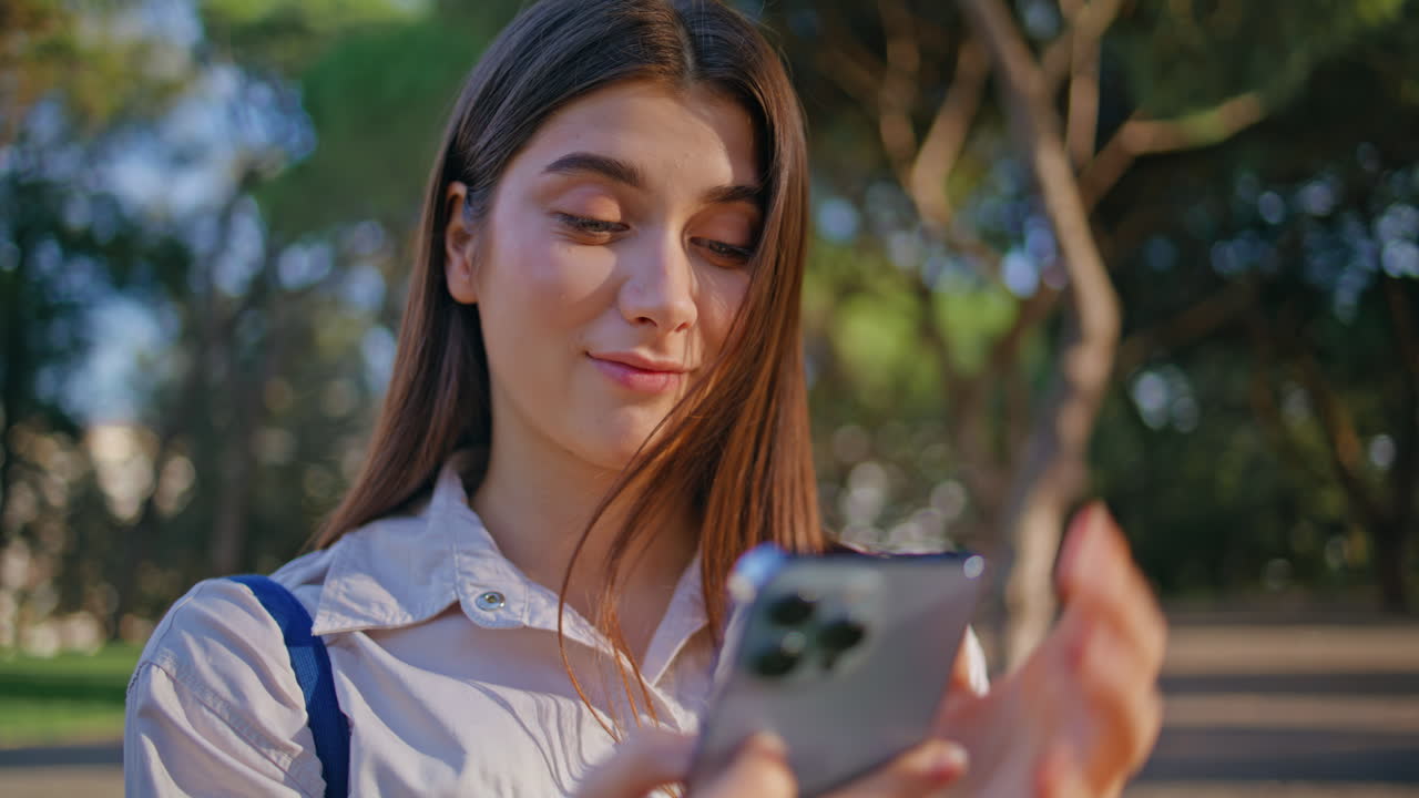 una mujer de negocios sonriente navegando por su teléfono inteligente en un parque verde vibrante de primer plano.