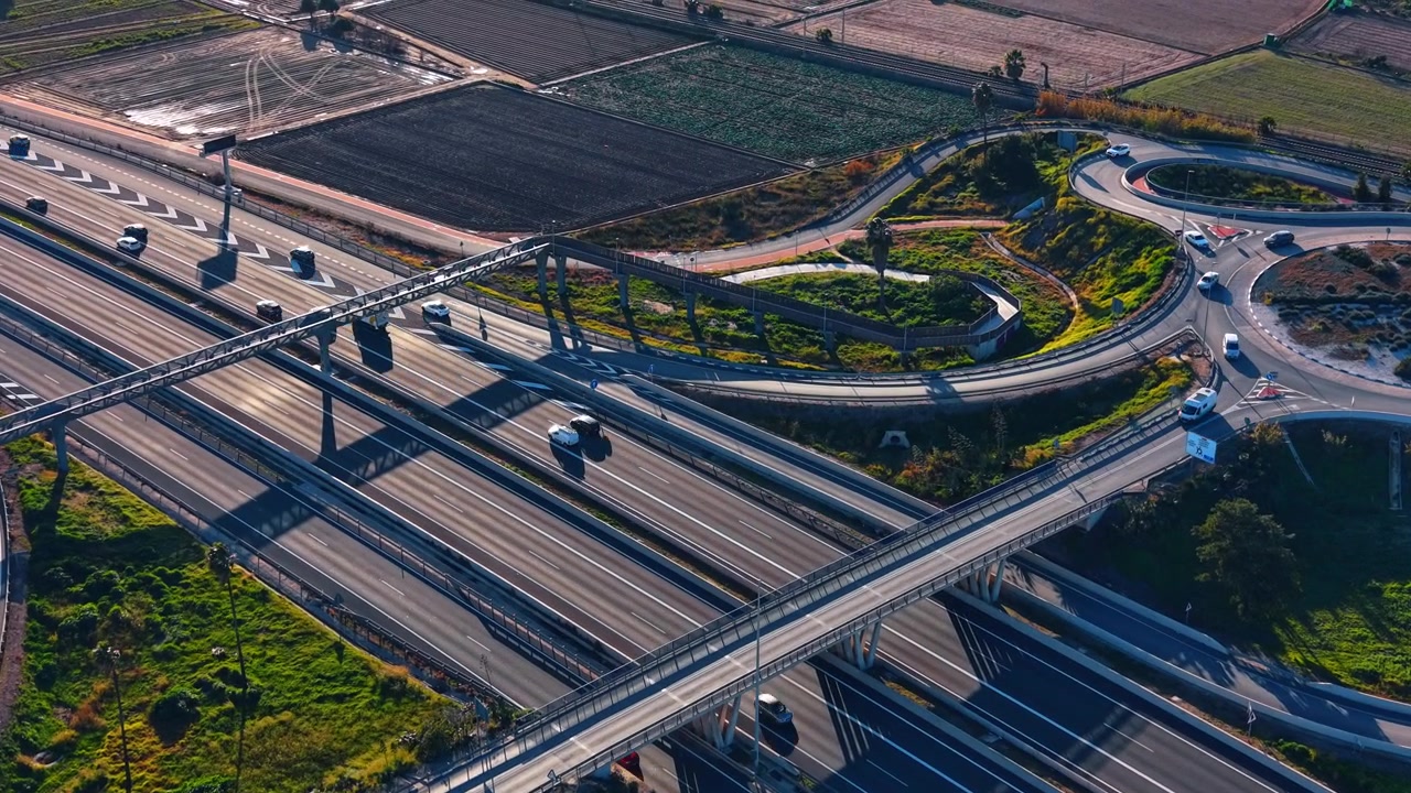 Aerial view of a multi lane highway interchange in Valencia, Spain. Drone perspective of asphalt roads, overpass bridge, green grass fields and moving cars.