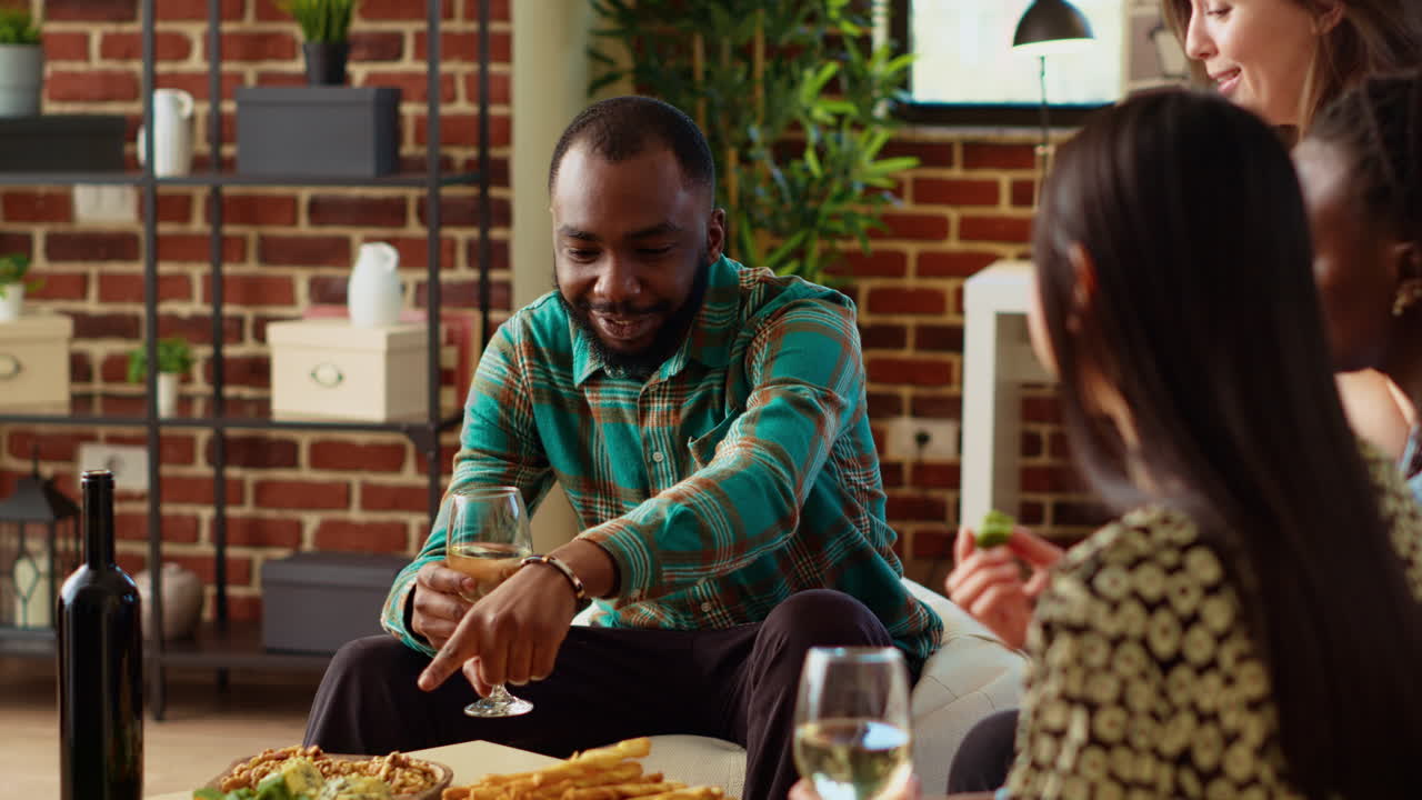 Happy host listening to engaging stories told by diverse group of friends in living room
