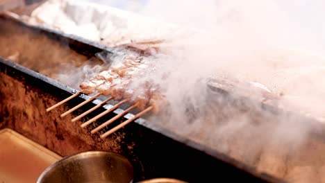hands flipping skewered meat on a smoky grill