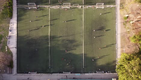 Toma-Aérea-De-Arriba-Hacia-Abajo-De-Jugadores-Jugando-Al-Fútbol-En-Tres-Campos-De-Fútbol-Durante-La-Luz-Del-Atardecer,-Lapso-De-Tiempo