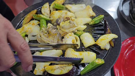 Man's-Hands-Frying-Chopped-Squid-on-Small-Grill-with-Okra-Plants-at-Local-Da-Lat-City-Restaurant,-Vietnam---close-up