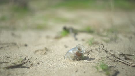 Eine-Flasche-Auf-Dem-Boden,-Festgesteckt-Im-Sand-Der-Anza-Borrego-Wüste,-Umgeben-Von-Zweigen-Und-Gras