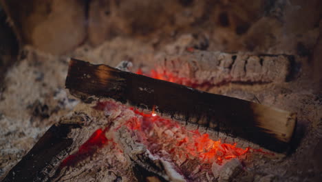 wood piece burns in hot ash pile at fireplace macro view