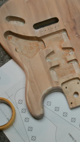 wooden blank of guitar body guitar neck blueprints and tools lie on the table wooden blank of guitar body guitar neck blueprints tools for manufacturing and laptop lie on the table modern workshop for musical instruments making concept of handicraft and small business