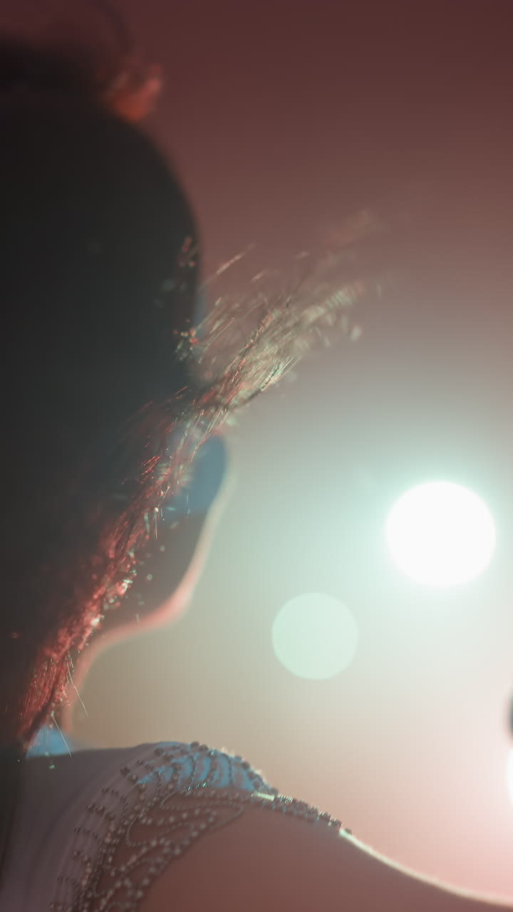 primer plano de una cantante con un vestido blanco y un micrófono vintage, en un fondo rosado. su cabello se mueve y las manos están en movimiento