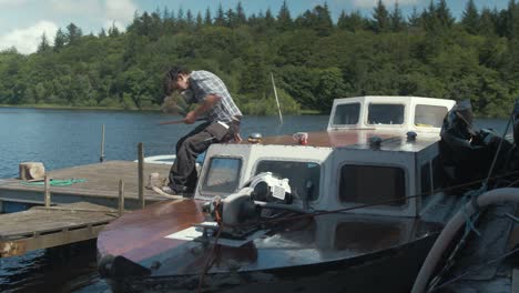 young man walks onto wood boat bow and checks teak wood trim for fit