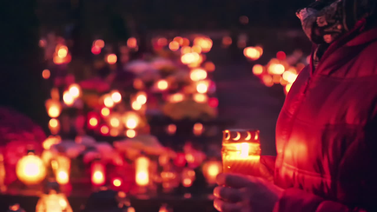 Donna con candela accesa che cammina in un cimitero di notte, le candele brillano nel buio