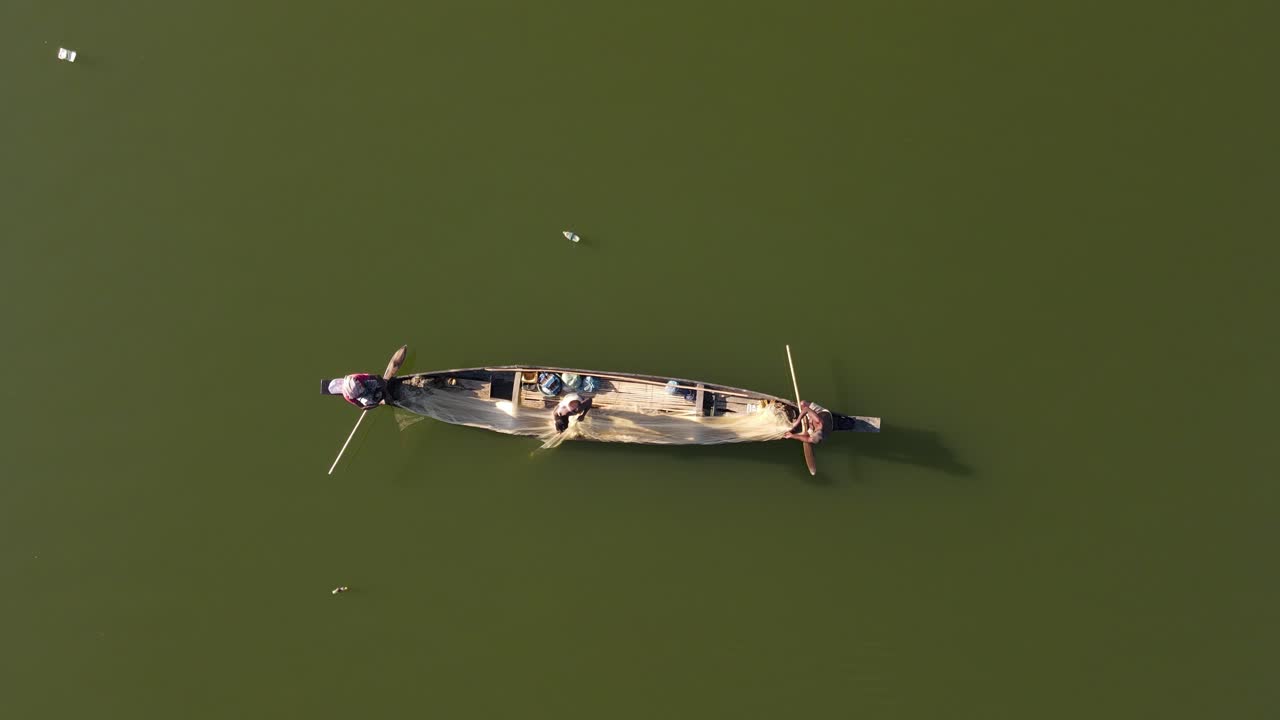 tres pescadores pescan con red en un río asiático mientras flota la contaminación plástica, destacando los impactos ambientales en las prácticas pesqueras tradicionales