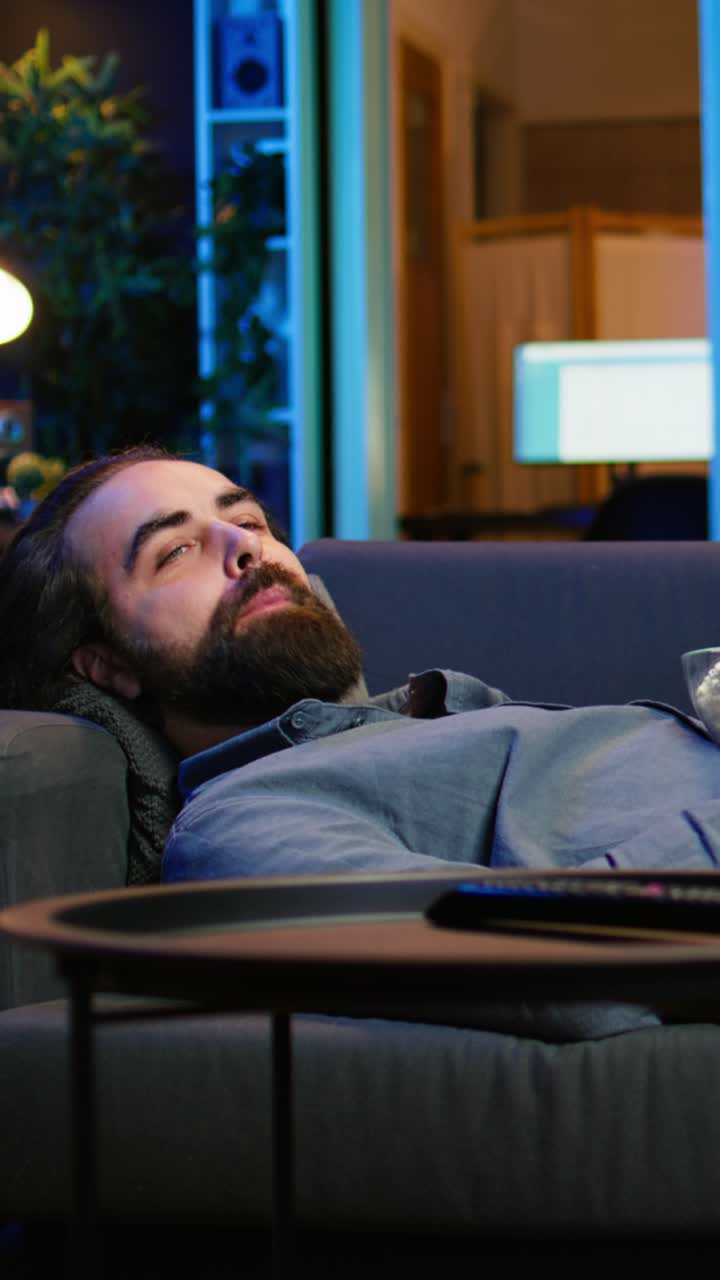 Vertical video Upbeat homeowner laying down on couch watching feel good movies on TV