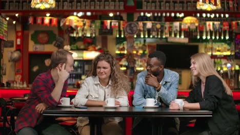 cheerful multi-ethnic company of friends in a restaurant drinking coffee talking and discussing telling stories about the university remembering funny moments.