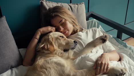 Close-up-shot:-a-blonde-girl-sleeps-in-bed-with-her-light-colored-dog-in-the-morning.-Happy-pet-owner