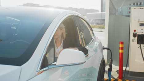 mujer conduciendo un coche eléctrico en una estación de carga