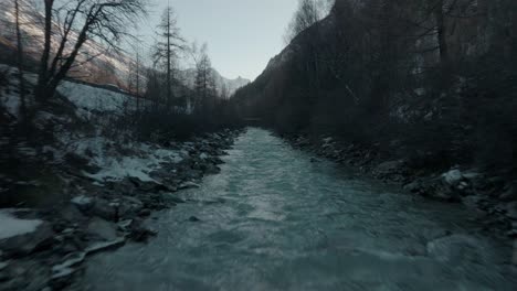 fast dolly over cold swiss flowing river water stream with snow on river banks in switzerland alps with epic mountain panorama