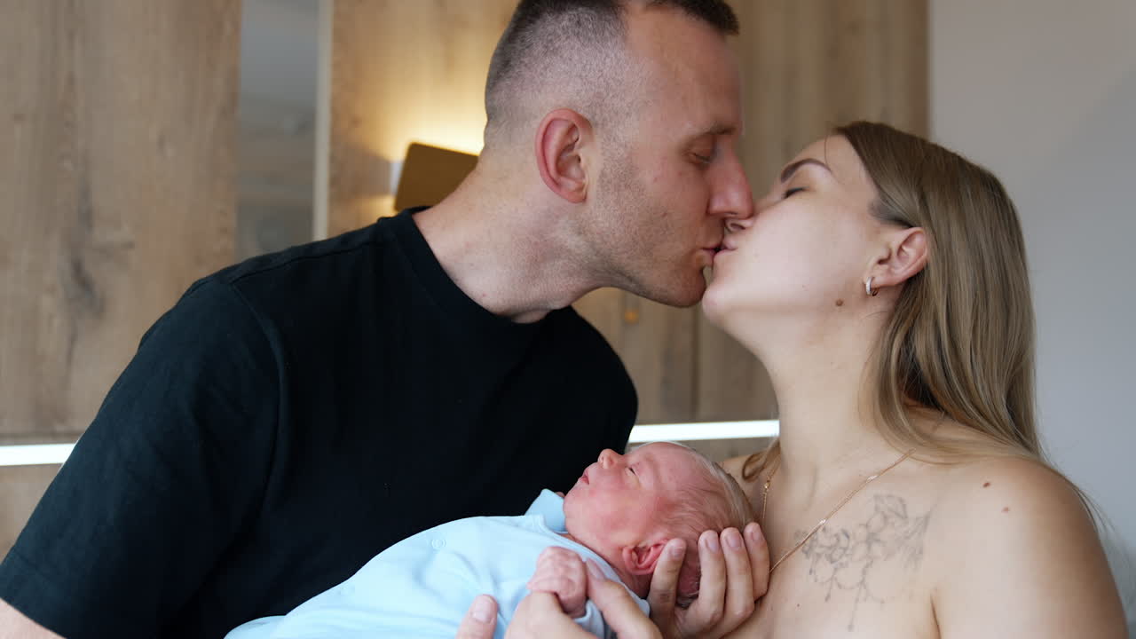 Happy Caucasian couple kissing. First time parents holding their newborn looking at it with love.