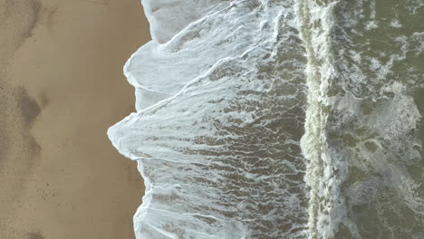 aerial shot slowly rising of a agitated sea and its powerful waves crashing on the beach