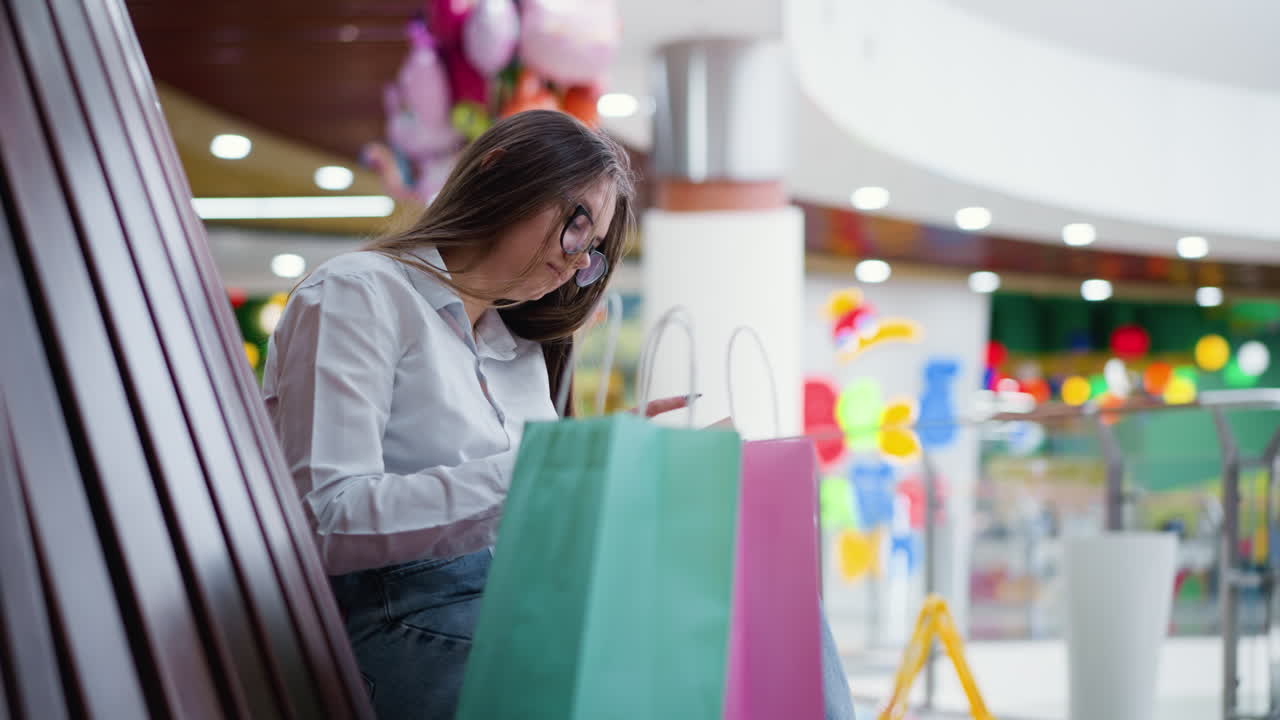 Primo piano di borse della spesa accanto a una giovane donna che legge un libro in un vivace centro commerciale con luci bokeh colorate, sfondo sfocato e calda illuminazione ambientale