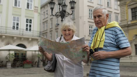 senior male and female tourists walking with a map in hands looking for route