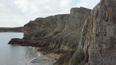 layered sea cliffs as aerial shot rises to reveal small enclosed bays and coastal erosion 4k wales uk