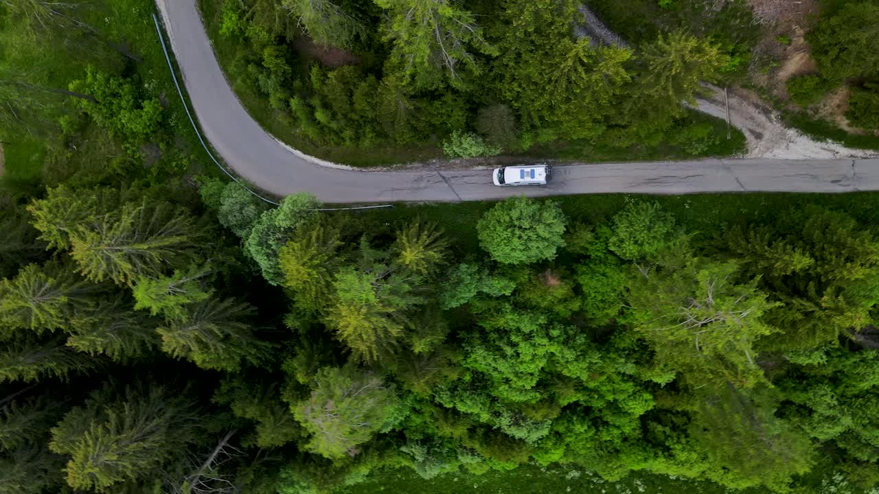 drone che vola dall'alto verso il basso dalla strada forestale europea con l'auto che scala le riprese aeree delle alpi