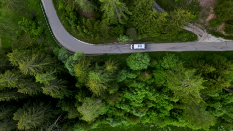 dron volando de arriba hacia abajo desde la carretera forestal de europa con un coche escalando las imágenes aéreas de los alpes