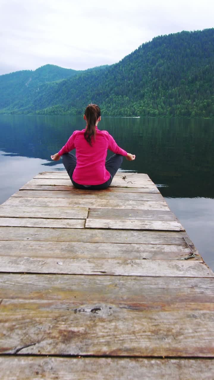 Donna che medita su un pontile di legno con vista su un lago e montagne