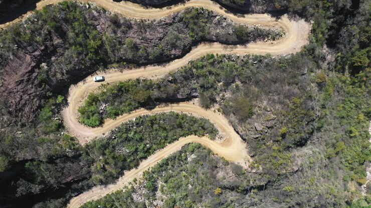 White car driving down winding mountain road, top down rising aerial