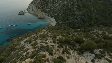 fpv drone view of cliffs and sailboats docked in cala d'egos beach, spain