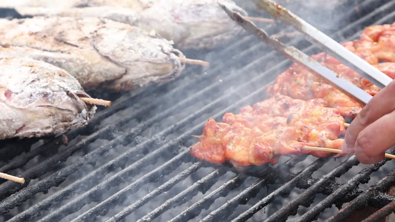 Close-up of skewered fish and meat being grilled over a charcoal barbecue.