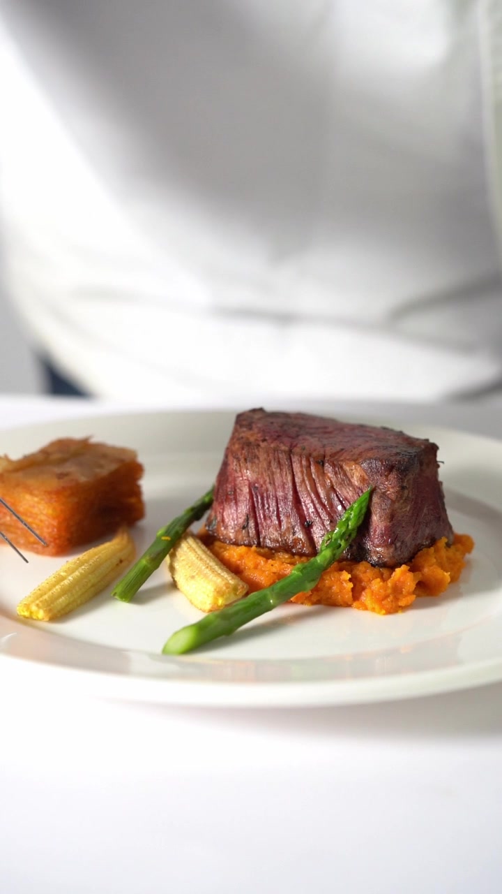A chief plating Juicy grilled beef steak served on creamy mashed vegetables in a minimalist plate, close up shot, insert shot