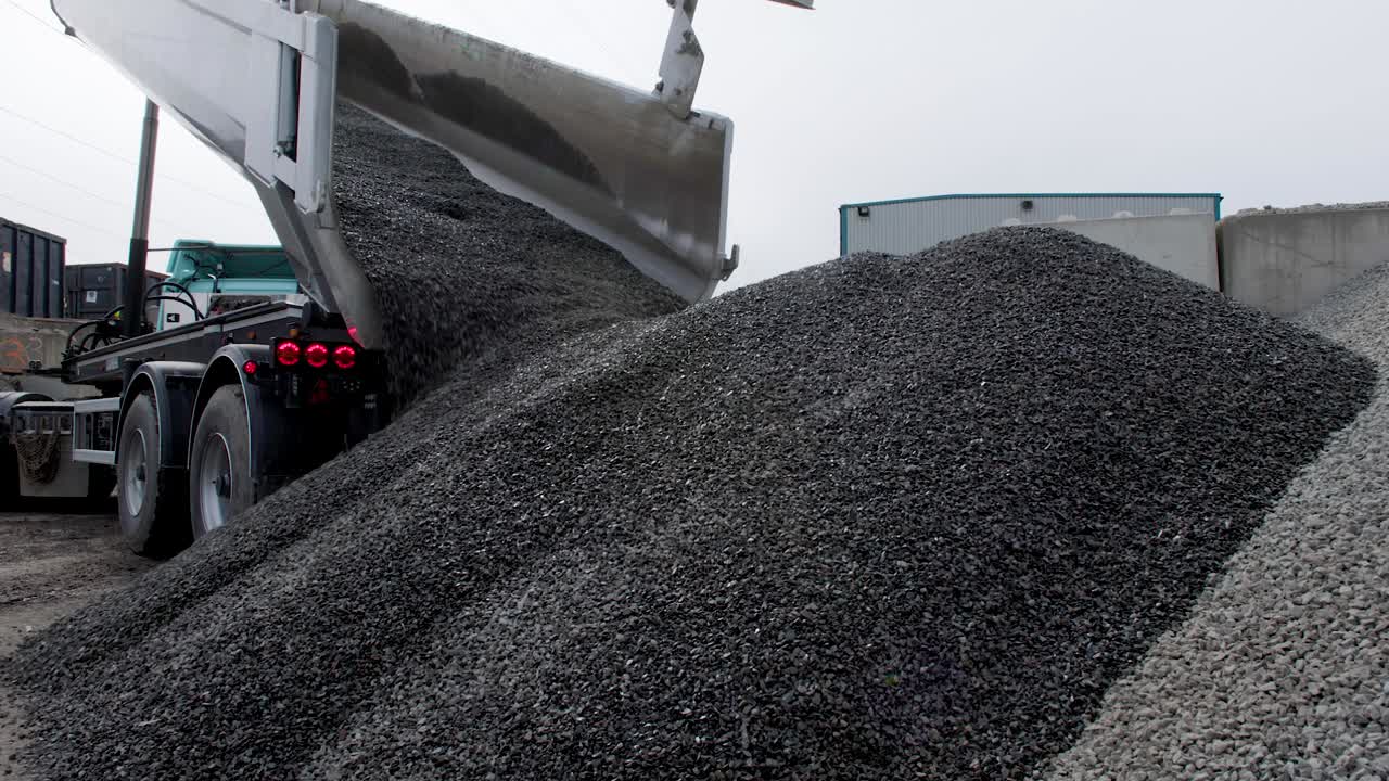 A tipper truck unloads and dumps a pile of gravel on the ground of construction site. Static shot low angle in 4k.
