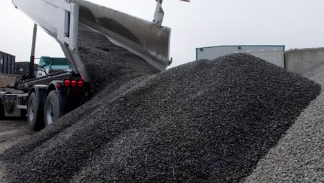 a tipper truck unloads and dumps a pile of gravel on the ground of construction site. static shot low angle in 4k.