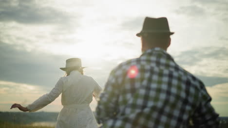 a close-up shot of a woman in a white dress and hat being chased by a man in a checkered shirt during sunset under a cloudy sky. the scene captures a dynamic and romantic moment with the sun