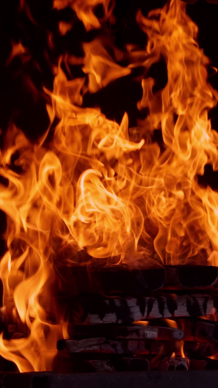 Pile of wooden logs burn with a good fire. Beautiful mesmerizing campfire burning at night. Close up. Vertical video.