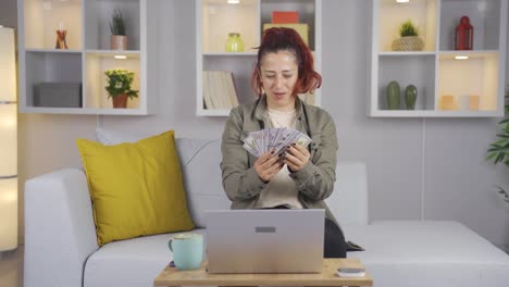 woman with dollars in hand at laptop rejoices.