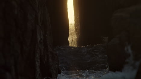 gold sunset sunlight ray shining through cave passage as ocean waves crash nanjjizal, cornwall